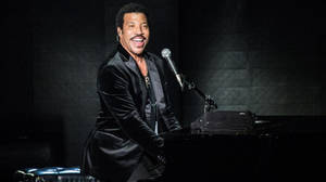 Lionel Richie 在音樂會期間在舞台上彈奏鋼琴並微笑。