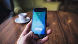 手拿著手機顯示Twitter登入畫面，旁邊有咖啡杯。