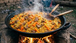 一大鍋米飯和肉在戶外明火上烹煮。