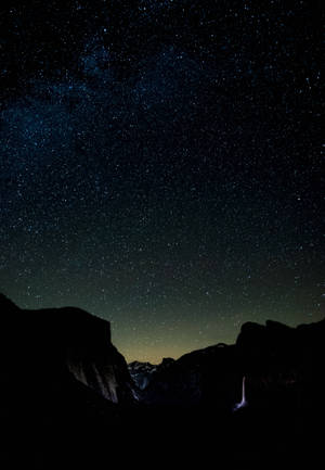 黑暗的山巒在繁星點點、帶有銀河的夜空下襯托著發光的瀑布。