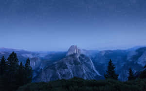 Half Dome 山在繁星點點的暮色天空下，前景有松樹