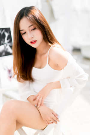 年輕女性身穿白色服裝坐在明亮房間的白色椅子上