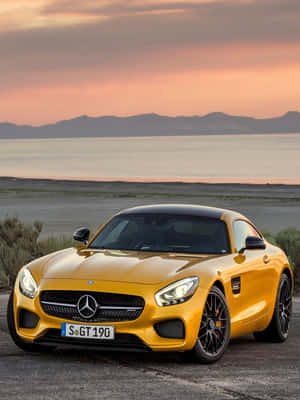 黃色 Mercedes-AMG GT 停泊在日落時分的湖邊，背景有山巒。 — 黃色 壁紙
