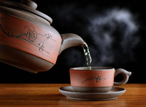 熱茶從陶瓷茶壺倒入木質表面上的相配茶杯中。