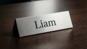 銀色名牌，上面刻有 Liam 的名字，置於深色木質表面。