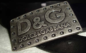 帶有鉚釘的銀色 Dolce & Gabbana 皮帶扣，放置在黑色皮革和白色布料上。 — 黑色動態圖 壁紙