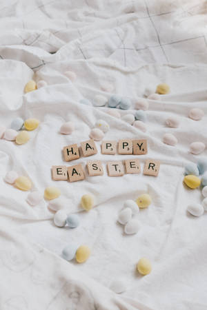 用 Scrabble 字母牌拼出的 Happy Easter 被粉彩蛋環繞，置於白色布料上。 — Huawei MatePad 11.5 S (2025) 壁紙