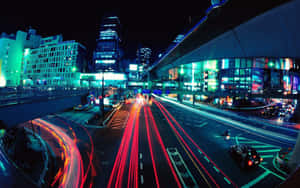 夜晚城市，繁忙高速公路上的汽車燈光在發光建築物下拉出線條。 — 極光 壁紙