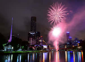煙火在夜間倒映在河流中的城市天際線上綻放。 — 節日 GIF 壁紙