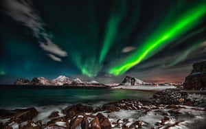 綠色北極光在夜晚照耀著白雪覆蓋的山脈和寧靜的大海。 — 2880x1800 壁紙