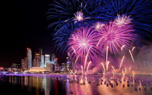 五顏六色的煙火在夜間水面上反射的城市天際線上綻放。 — 新年快樂 GIF 壁紙