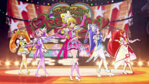 五位動漫女孩在充滿活力的舞台上跳舞，伴隨著發光的燈光和節日背景。 — 音樂 GIF 壁紙