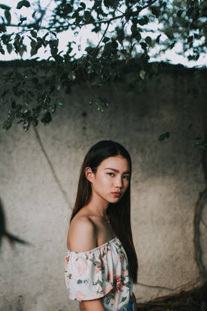 年輕女性穿花卉上衣站在混凝土牆附近的樹枝下