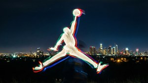 夜間，籃球運動員持球跳躍，在明亮的城市景觀中留下的光跡。 — Jordan 標誌 GIF 壁紙