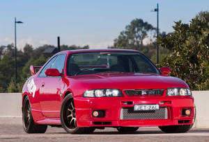 紅色日產Skyline R34跑車停泊在戶外，靠近樹木和街燈。
