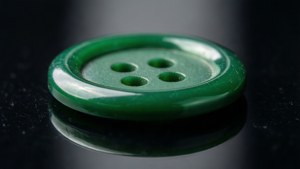 一顆在深色反光表面上的綠色四孔鈕扣。