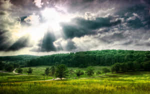 陽光穿過暴風雲，照耀在一個有樹木和丘陵的綠色山谷上。