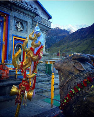金色三叉戟和石牛雕像在喜馬拉雅寺廟，背後是雪峰。