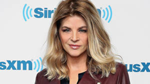 在SiriusXM活動中，身穿栗色外套的女性對著鏡頭微笑。