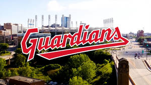 棒球場帶有 Guardians 標誌，位於有綠樹和道路的城市中。 — 蝙蝠俠標誌 壁紙