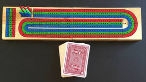 深色桌子上放著木製克里比奇棋盤、棋子和一副撲克牌。
