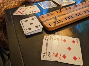 深色桌子上的克里比奇棋盤和撲克牌，附近有一張柳條椅。