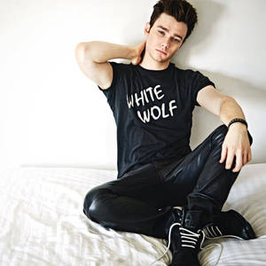 年輕男子穿著黑色「White Wolf」T恤和皮褲坐在白色床上。 — 基斯保羅 壁紙