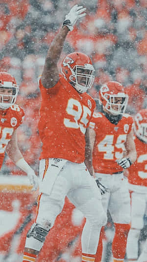 身穿橙色球衣的足球員在雪中比賽向人群揮手。 — NFL 美式足球 GIF 壁紙