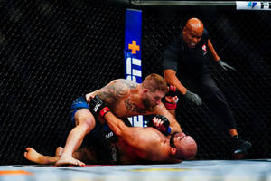 兩名MMA拳手在UFC八角籠內纏鬥，裁判在旁觀看。