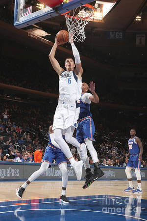 NBA比賽中，身穿白色球衣的籃球球員在藍色球衣防守球員上方入樽。