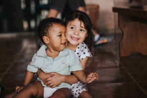 兩個快樂的幼兒在室內木地板上擁抱。