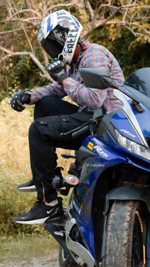 身穿格仔襯衫和頭盔的電單車手，坐在草地戶外環境中的藍色Yamaha R15電單車上。