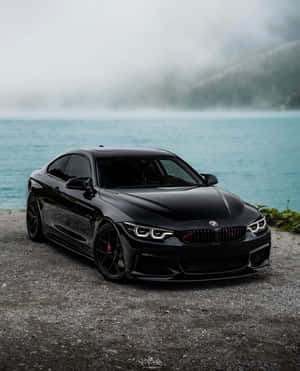 黑色BMW M4雙門轎跑車停泊在霧氣瀰漫的湖邊，背景有樹木繁茂的山丘。
