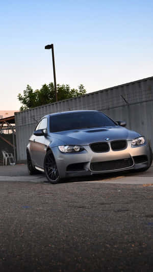 黃昏時分，銀色BMW M3跑車停在瀝青路上，靠近圍欄。