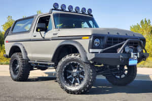 升高嘅灰色福特Bronco，黑色車輪同車頂燈，停泊喺行人路上。