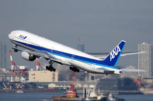 ANA飛機在水面上起飛，背景有城市和起重機。