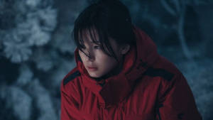 年輕女子身穿紅色冬季外套站在夜晚的雪地森林中