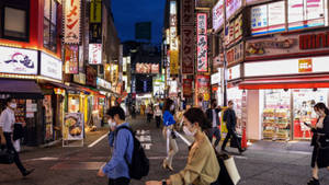 戴著口罩的人們在夜晚走過東京一條充滿活力的霓虹燈小巷，頭頂是發光的招牌。