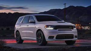 白色Dodge Durango SRT SUV在黃昏時分停泊，背景有山脈和遠處燈光。 — 汽車 壁紙