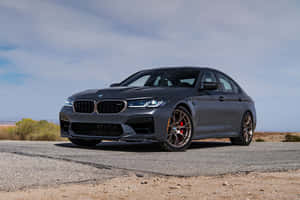 啞光灰色BMW M5運動轎車配備青銅輪圈，停在日落時分的沙漠路上。