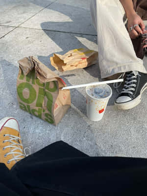 兩個人在行人路上吃快餐，旁邊有運動鞋和紙袋。 — 麥當勞 壁紙