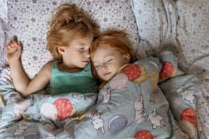兩個年幼的孩子在有圖案的毯子下並排睡覺。 — 露營 壁紙