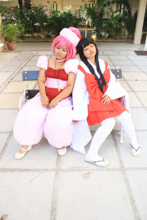 兩位穿著色彩繽紛服裝的動漫cosplayer在庭院長椅上休息。 — iPhone Duo 壁紙