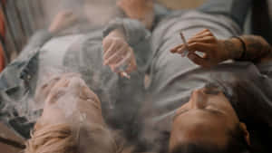 兩個人躺著吸煙，煙霧環繞他們的臉龐。 — 煙霧動畫 壁紙