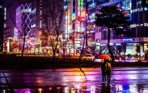 兩個人拿著橙色雨傘在夜間霓虹燈照亮的城市街道上雨中行走。