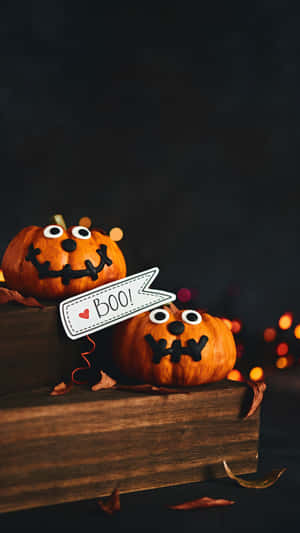 兩個微笑的萬聖節南瓜，有凸眼和一個 'BOO!' 標誌在木箱上。 — 南瓜 壁紙