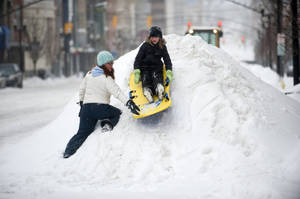 女性在積雪街道上推著小孩坐黃色雪橇於雪堆頂端。 — 雪 壁紙