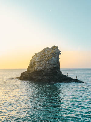 兩個人喺岩石島上日落時分，平靜嘅海水 — 島嶼 壁紙