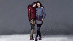 兩個穿著冬季外套的女人在雪中站立，正值下雪。 — 冬日美學 壁紙