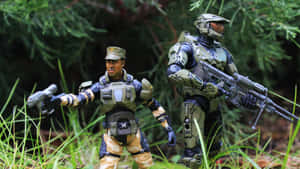 兩個穿著軍事和未來風格盔甲的可動人偶站在長滿草的森林中。 — 驚奇隊長 壁紙